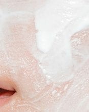 A close-up of a person's face with a thick layer of white facial mask applied, covering the skin around the nose and mouth area.