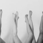 A black-and-white photo of multiple pairs of legs raised in the air, showing feet and lower legs against a plain background.