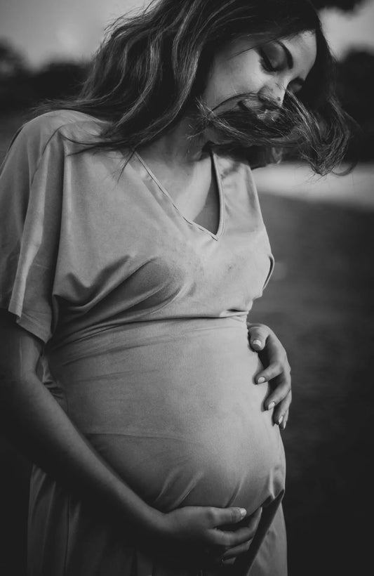 Pregnant woman in a loose dress cradling her baby bump in a black-and-white outdoor setting.